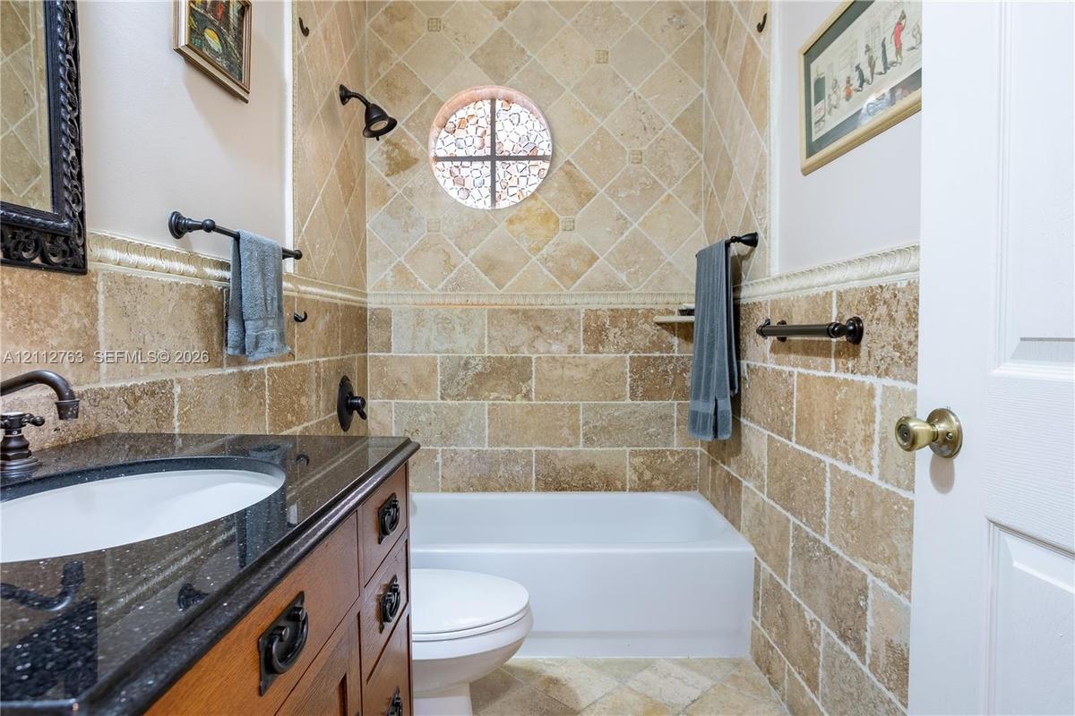 Bathroom featuring natural stone tile walls in a combination of brick-set and diagonal patterns, dark stone-finish vanity countertop, wood-finish cabi