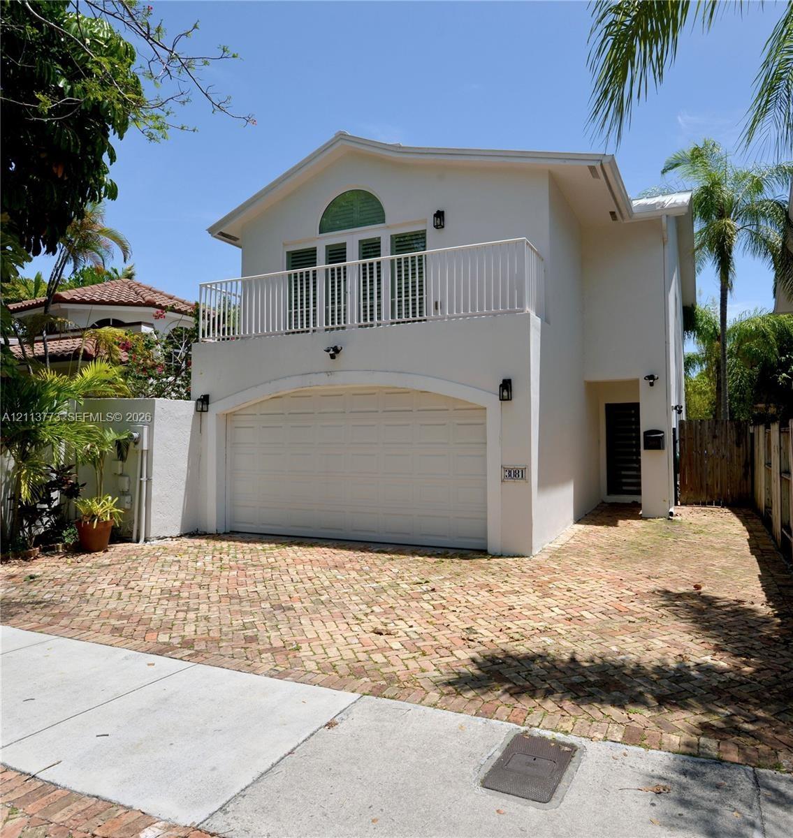 Two-story exterior featuring a brick-paved driveway, an arched garage entry, a second-story balcony with metal railing, and a decorative arched window