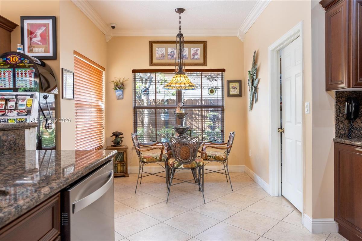 Eat-in kitchen featuring crown molding, ceramic tile flooring, stone-finish countertops, dark wood cabinetry, and a tiered stained-glass pendant light