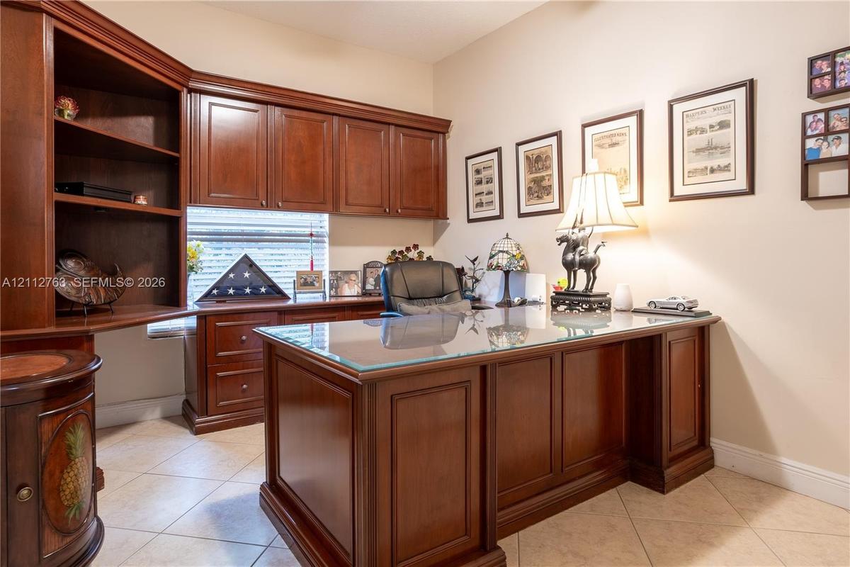Custom built-in wood cabinetry featuring upper storage units, open shelving, and integrated desk surface with drawer storage, finished with tile floor