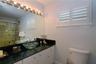 Vanity featuring a dark stone countertop, glass vessel sink, white cabinetry, integrated full-width mirror with multi-bulb light fixture, and plantati