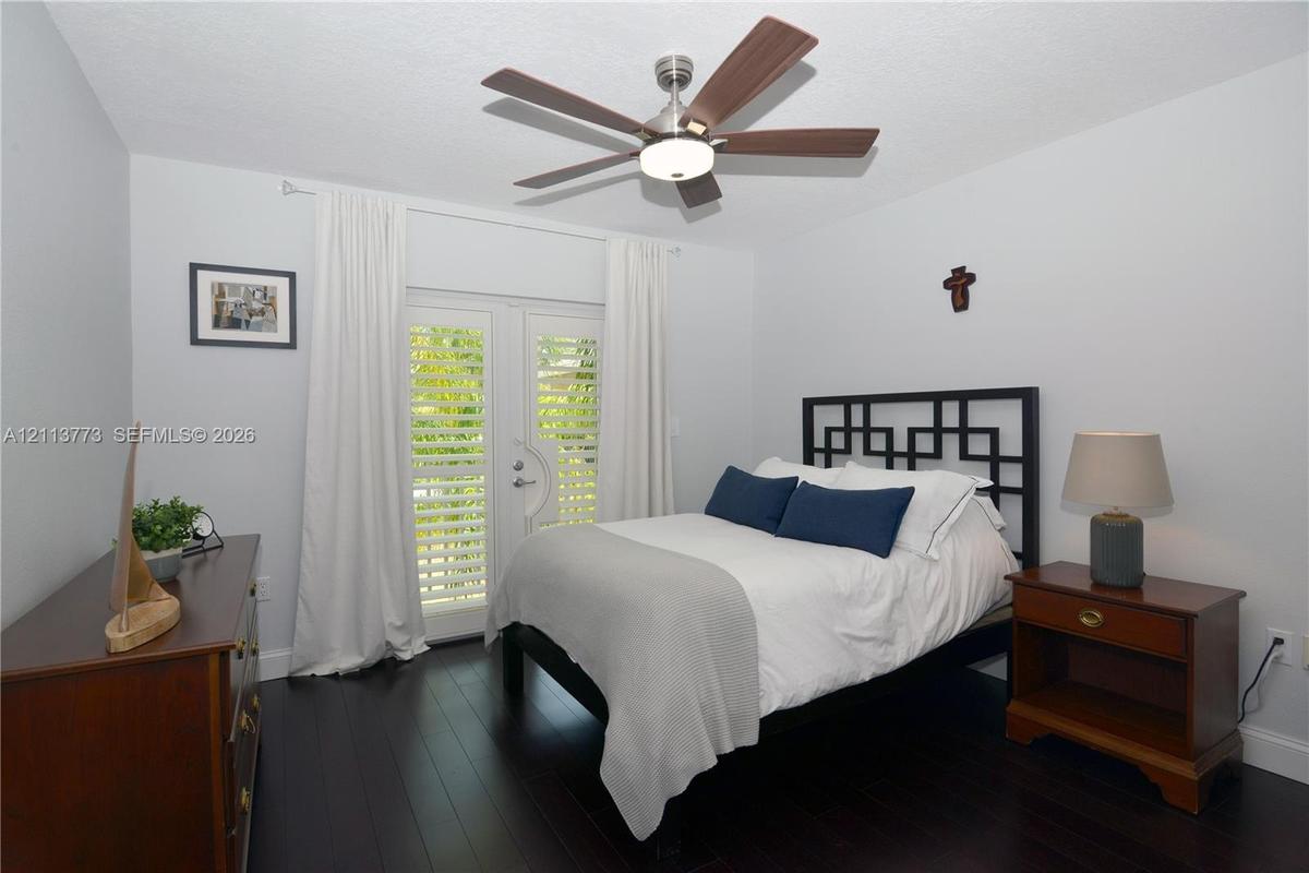 Wood-finish flooring, ceiling fan with integrated lighting, and glass-paned French doors with plantation shutters