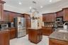 Kitchen featuring stained wood cabinetry, stone-surface countertops, tile flooring, stainless steel appliances, and a suspended metal pot rack