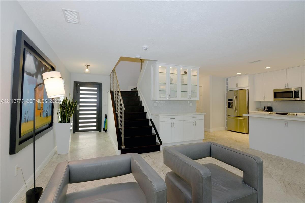 Modern entryway featuring a multi-paneled glass front door, stone-finish flooring, and a staircase with dark treads and metal railings