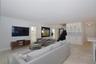 Open-concept interior featuring light stone-finish flooring, white built-in cabinetry with glass display uppers, and a custom staircase with metal rai