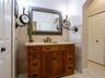 Custom wood vanity with multi-drawer storage, stone countertop, integrated vessel sink, wall-mounted swing-arm vanity mirrors, and stone-tiled wainsco