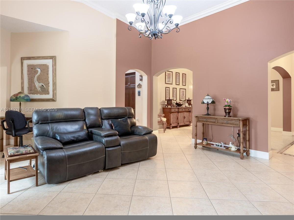 High vaulted ceilings featuring a multi-arm chandelier, neutral ceramic tile flooring, and decorative arched entryways