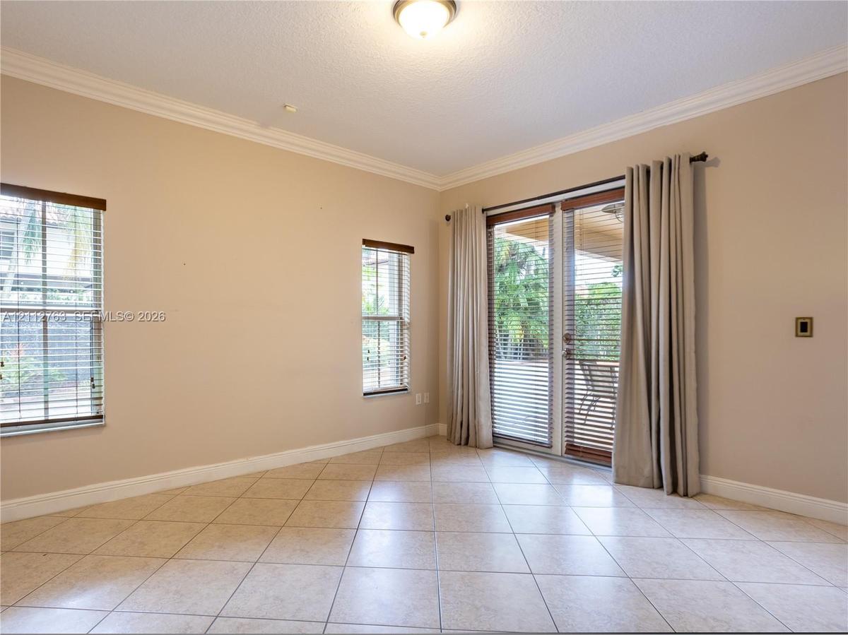 Neutral-toned interior featuring large-format tile flooring, crown molding, double glass-paneled exterior doors, and windows with integrated blinds