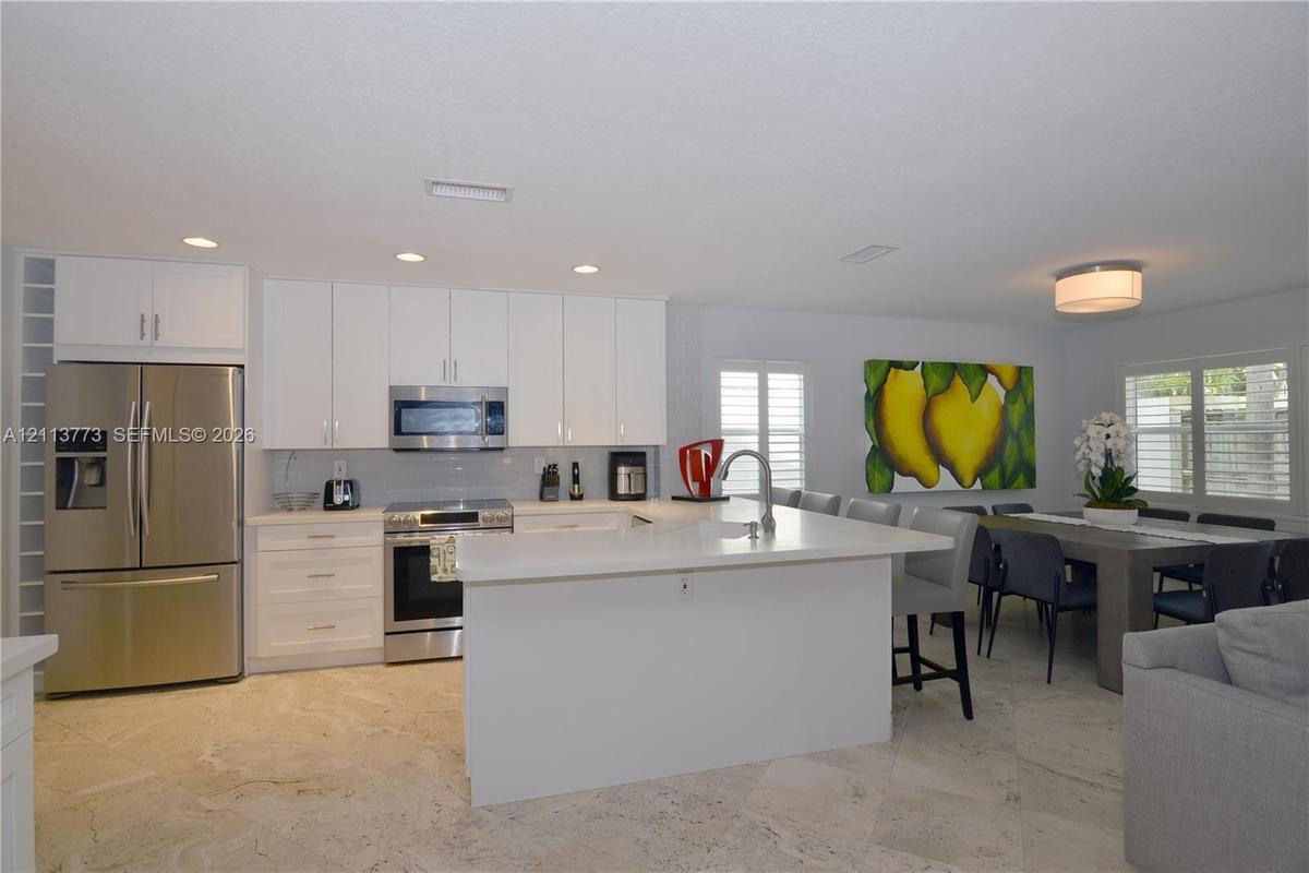 Kitchen featuring white cabinetry, stone-finish island with integrated sink, stainless steel appliances, recessed lighting, and stone flooring