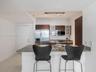 Kitchen featuring a stone countertop peninsula, stainless steel refrigerator and built-in microwave, flat-panel wood-finish cabinetry with glass-front
