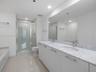 Double vanity featuring a stone-finish countertop, undermount sinks, contemporary cabinetry with metal hardware, and an expansive wall-to-wall mirror