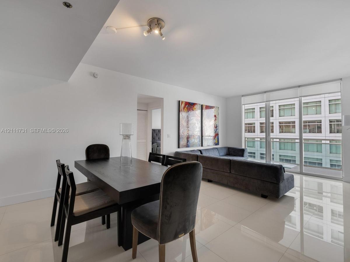 Open-concept interior featuring large-format tile flooring, recessed lighting, and floor-to-ceiling windows with sliding glass door access to a balcon