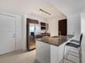 Kitchen featuring stone-surfaced countertops, a center island with an integrated sink, dark wood-finish cabinetry, stainless steel appliances, and tra