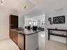 Kitchen featuring a stone-surface island, undermount sink with a gooseneck faucet, stainless steel dishwasher, full-height dark-toned cabinetry, and p