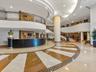 Grand lobby featuring expansive radial-patterned stone flooring, a curved reception desk with wood paneling, a sweeping staircase with ornate metal ra