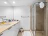 Bathroom featuring a wide vanity with high-gloss white cabinetry, a stone-surfaced countertop, a wall-to-wall mirror, and a walk-in shower enclosure w