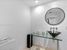 Glass-topped vanity featuring a conical vessel sink, wall-mounted faucet, and minimalist circular mirror