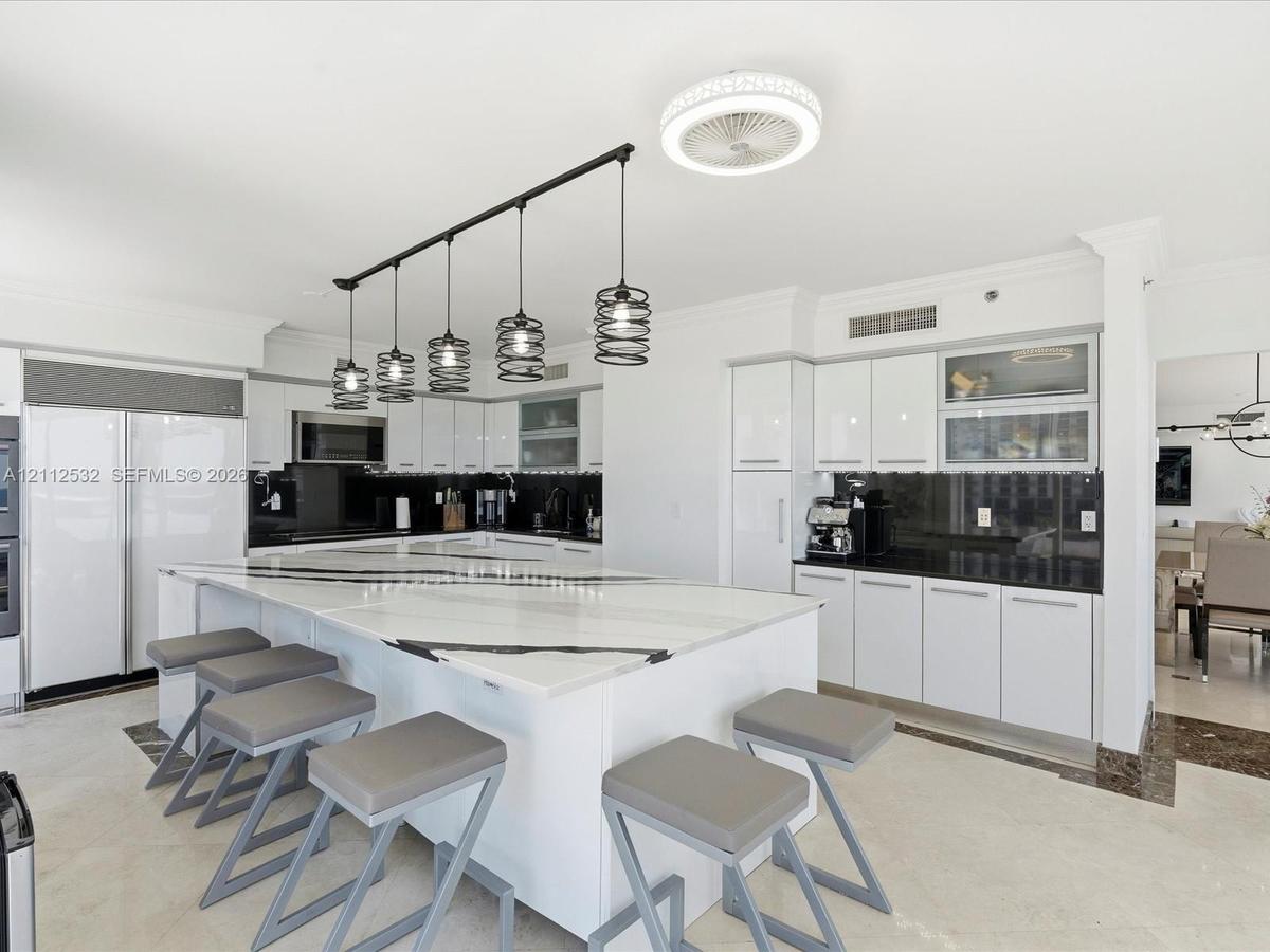 Kitchen featuring a large waterfall-edge island, high-gloss white cabinetry, contrasting dark stone countertops, integrated stainless steel appliances