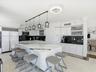 Kitchen featuring a large waterfall-edge island, high-gloss white cabinetry, contrasting dark stone countertops, integrated stainless steel appliances