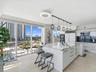 Kitchen featuring high-gloss cabinetry, stone-topped center island with waterfall edge, built-in double wall ovens, five-light linear pendant fixture,