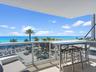 Covered balcony featuring glass railing, stone flooring, and expansive ocean scenery