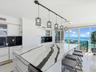 Kitchen featuring a large central island with veined stone countertop, high-gloss white cabinetry, black tile backsplash, and linear pendant lighting,