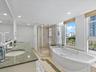 Dual-sink vanity with natural stone countertop, corner glass-enclosed shower, deep soaking tub, tile flooring with stone inlay, and large windows with