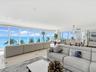 Open-concept living space featuring floor-to-ceiling glass windows, polished stone flooring, and expansive ocean and coastal scenery