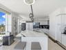 Kitchen featuring a substantial waterfall-edge island with stone countertop, flat-panel white cabinetry, built-in stainless steel appliances, multi-pe