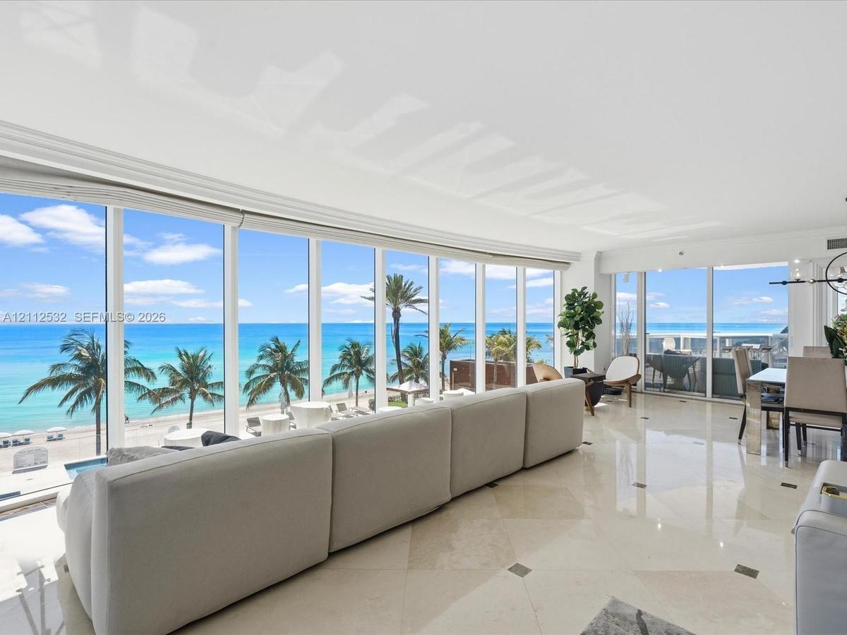 Floor-to-ceiling windows, polished stone tile flooring with decorative inlay, and coastal scenery