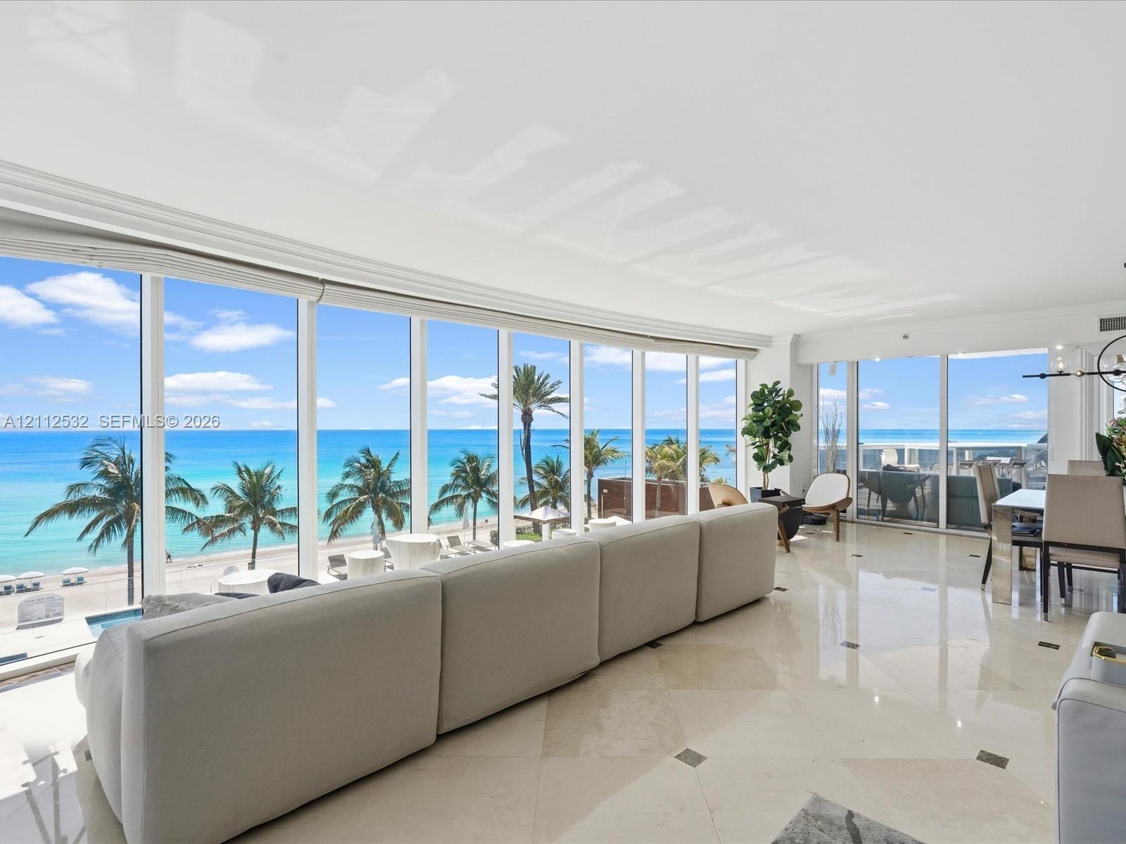 Floor-to-ceiling windows, polished stone tile flooring with decorative inlay, and coastal scenery