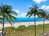 Direct waterfront exposure featuring a sandy beach, turquoise ocean waters, and mature palm trees