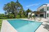 Modern exterior featuring a swimming pool, integrated spa, stone-paver decking, and a covered lanai with a wood-finished ceiling