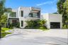 Modern architectural exterior featuring a smooth stucco facade, upper-level terrace with glass railing, decorative circular paver hardscaping, and a m