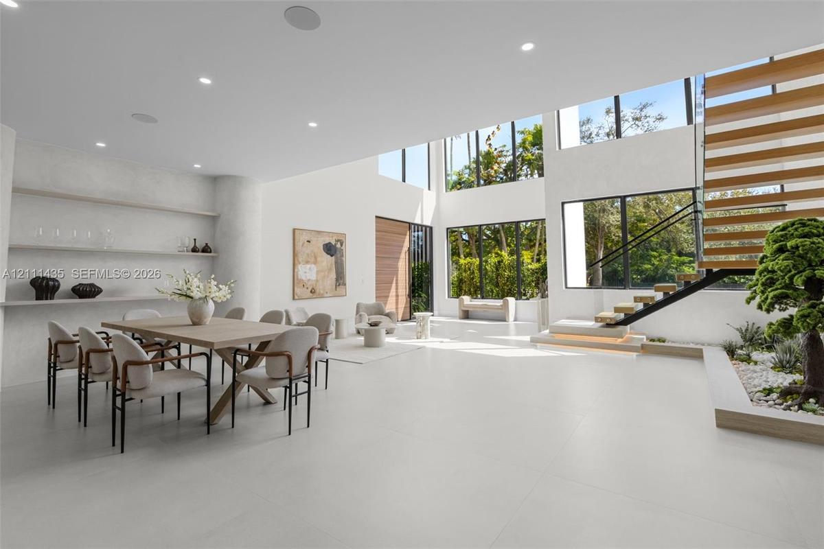 Double-height living area featuring large-format tile flooring, floor-to-ceiling windows, custom built-in recessed shelving, and a floating staircase 