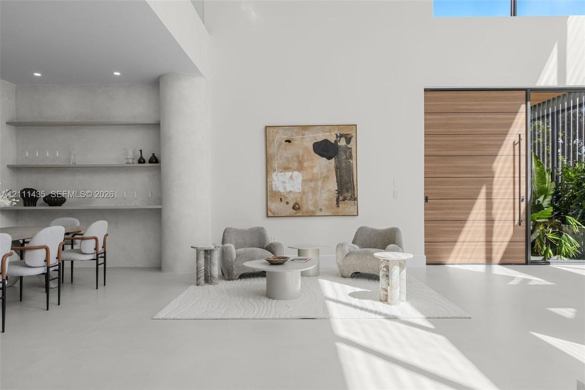 Double-height ceiling with recessed lighting, integrated stone shelving, polished concrete flooring, oversized wood-finish front entry door, and floor