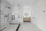 Walk-in shower with frameless glass enclosure, rainfall shower head, and stone-tile surround, paired with a floating wood-finish vanity featuring an i