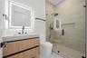 Floating wood-finish vanity with a rectangular sink, integrated LED-backlit mirror, walk-in shower with a glass enclosure and built-in recessed shelvi