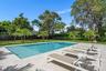 Rectangular swimming pool with integrated sun shelf and spa, surrounded by stone-finish paver decking, expansive grass lawn, mature trees, and privacy