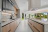 Kitchen featuring light wood-finish cabinetry, stone countertops, integrated under-cabinet lighting, a contemporary ceiling-mounted range hood, and la