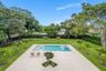 Expansive backyard featuring an in-ground swimming pool, light-toned concrete patio, manicured lawn, perimeter fencing, and mature trees