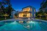 Modern two-story residence featuring a smooth stucco exterior, a covered patio with recessed lighting, a second-level balcony with a glass railing, an