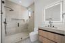 Bathroom featuring a floating wood-finish vanity, integrated stone-composite countertop, illuminated mirror, walk-in shower with floor-to-ceiling tile