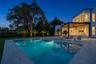 Modern architectural exterior featuring a swimming pool with integrated stairs, expansive stone paver pool deck, covered patio with wood-paneled ceili