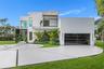 Modern two-story exterior featuring smooth stucco siding, a second-level balcony with glass railing, tiered concrete driveway with decorative inlay, a