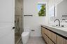 Floating vanity with wood-finish cabinetry, rectangular integrated sink, matte black hardware, glass-enclosed shower, and illuminated mirror