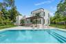 Modern two-story residence featuring a smooth stucco exterior, expansive concrete patio, built-in swimming pool with step entry, and a covered pavilio