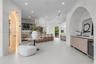 Open-concept floor plan featuring arched architectural entryways, a climate-controlled glass wine cellar, custom light wood cabinetry, and recessed li