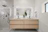 Floating wood-finish vanity with dual sinks, stone-surface countertop, LED-backlit mirror, and matte black fixtures, paired with a walk-in shower feat
