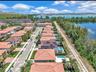 Aerial perspective of residential neighborhood featuring tile-roofed structures, solar panel arrays, private swimming pools, and waterfront placement
